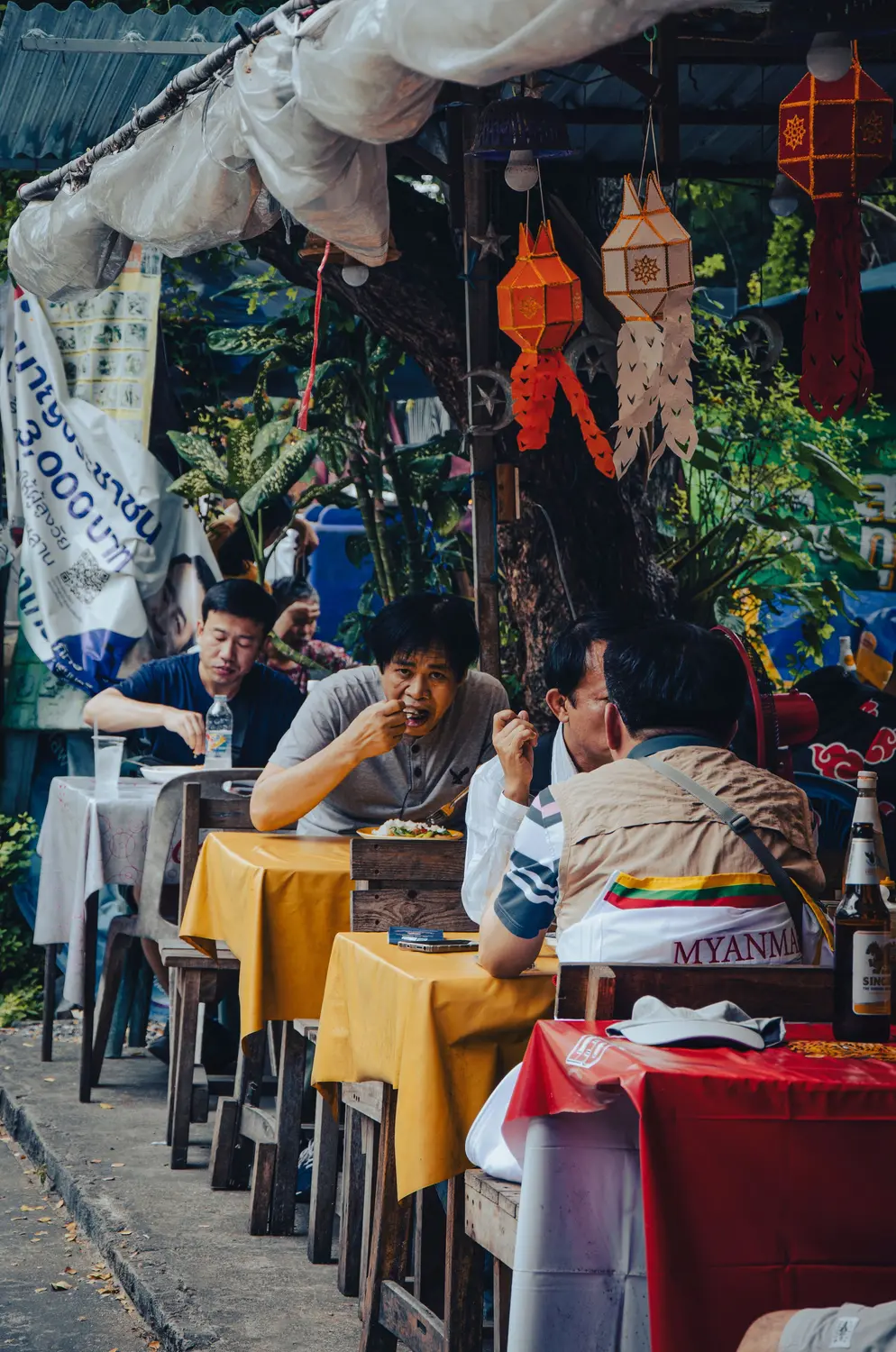 Local men eating at outdoor street food restaurant with decorative paper lanterns hanging overhead, Mandalay Myanmar
