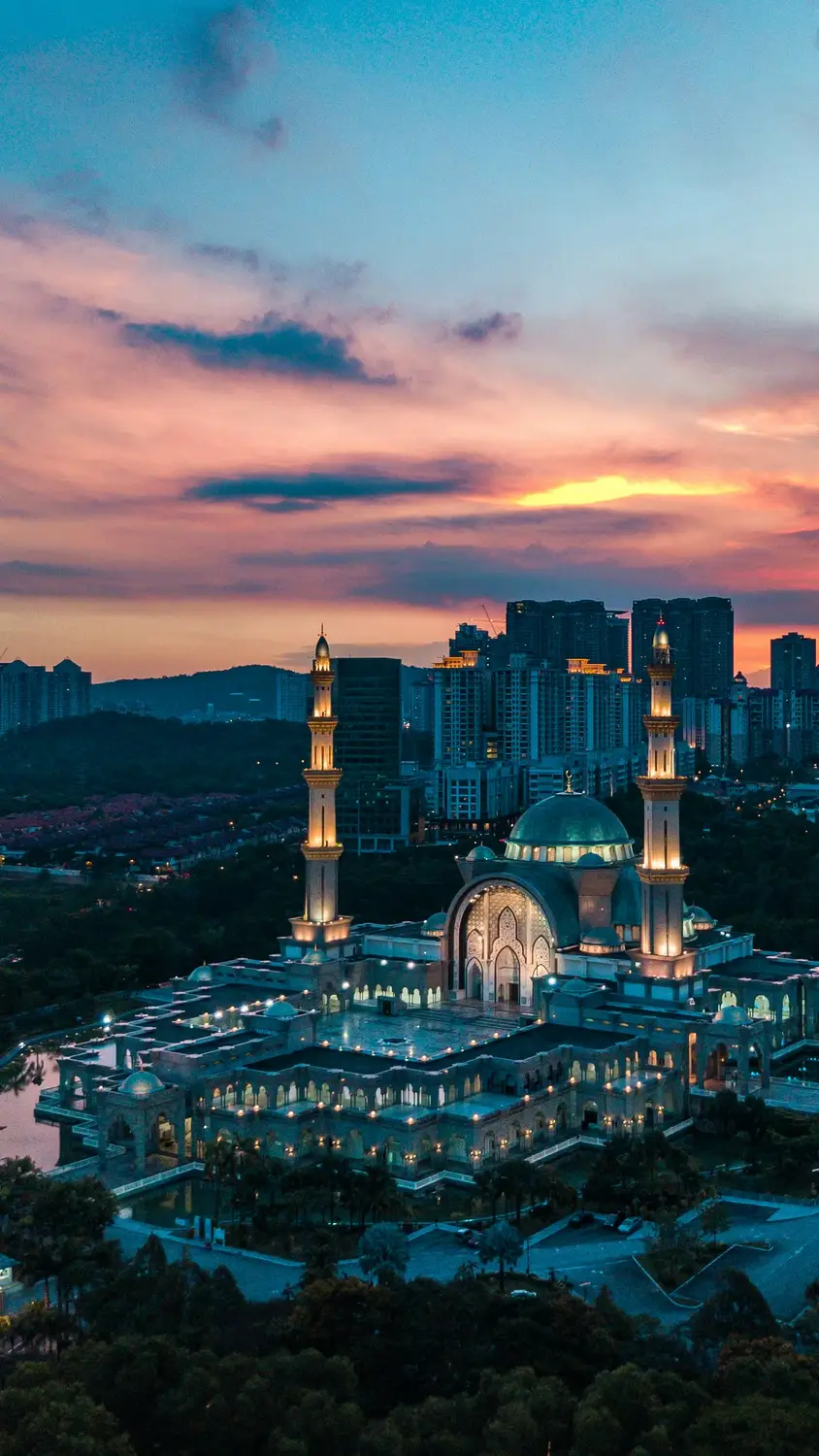 Aerial view of Masjid Wilayah Persekutuan mosque illuminated at sunset with colorful pink and orange sky and Kuala Lumpur city skyline Malaysia
