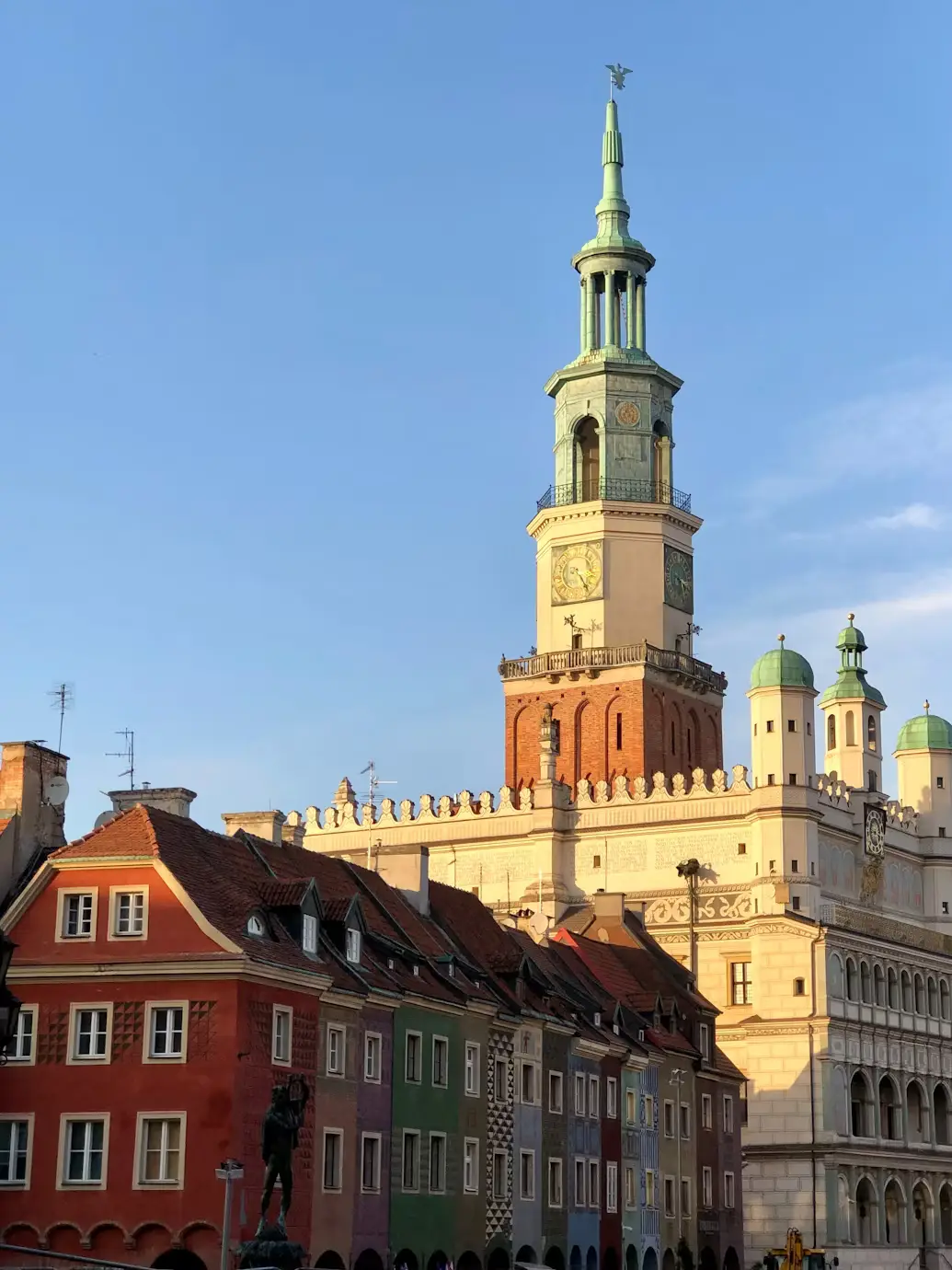 Historic Polish city square with colorful buildings and a tall ornate church tower against a clear blue sky.