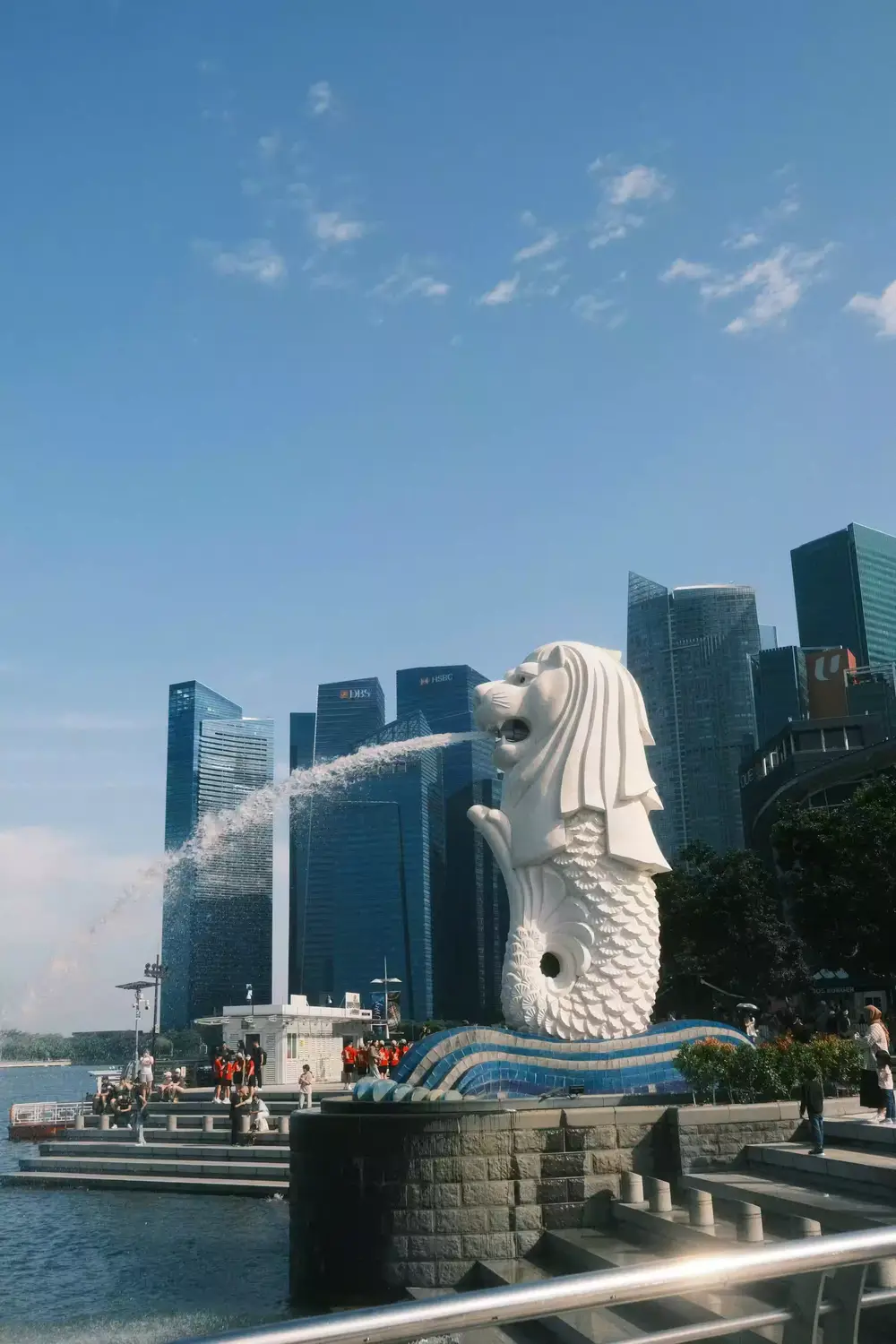 Merlion statue spouting water at Merlion Park with Singapore CBD skyline and DBS HSBC skyscrapers in the background