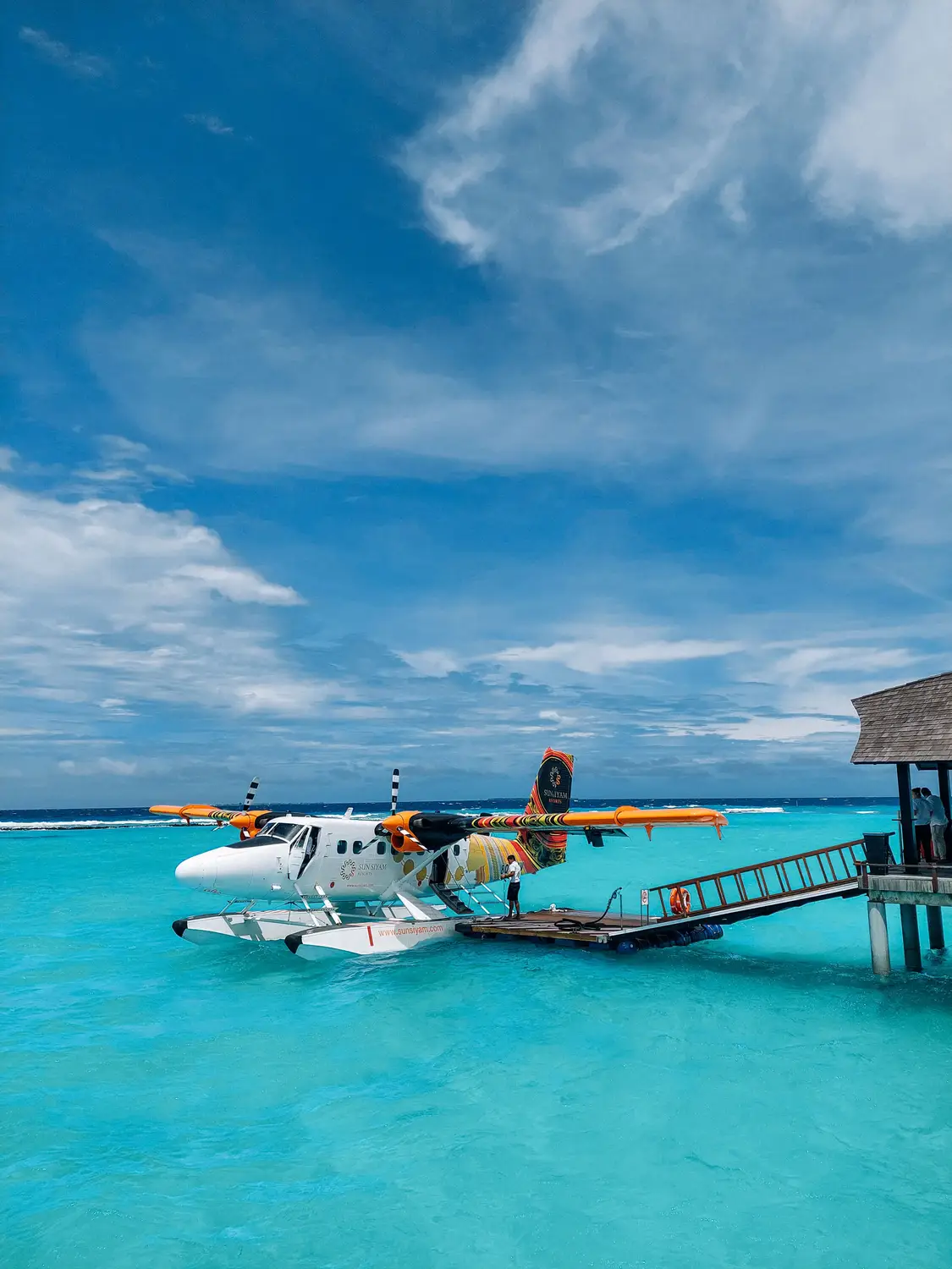 Seaplane docked at wooden overwater jetty pier with turquoise lagoon and blue sky at Maldives island resort transfer