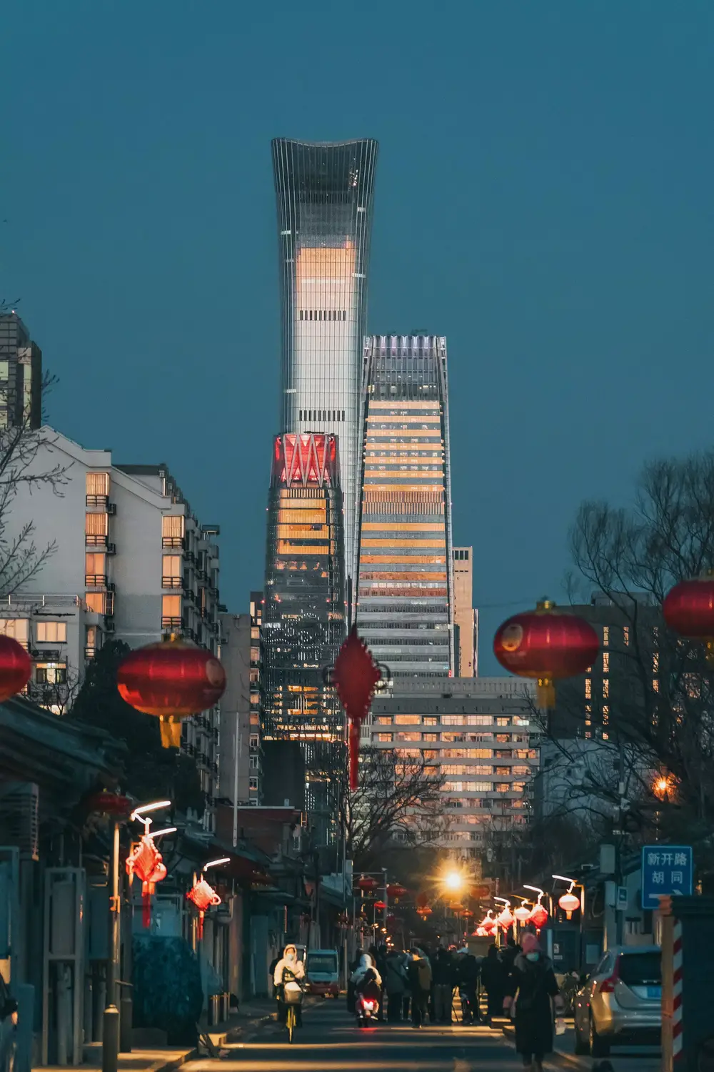 Beijing hutong street at dusk with red lanterns and CITIC Tower skyscraper in background, China