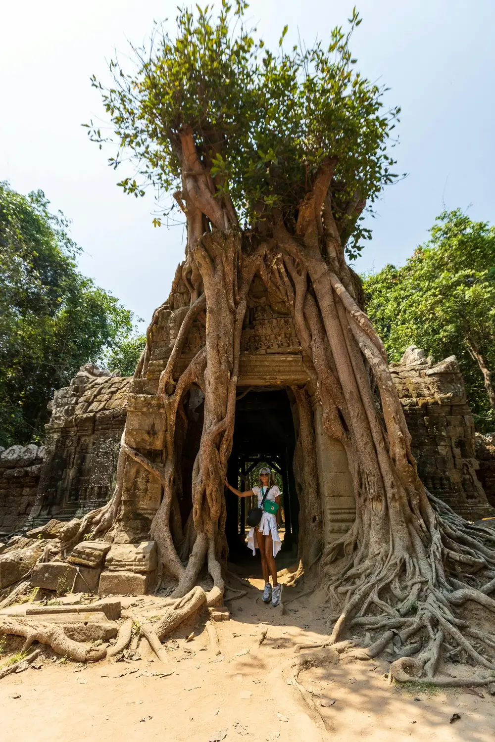 Female tourist standing inside ancient stone temple doorway overgrown with massive banyan tree roots at Ta Som temple, Angkor, Cambodia