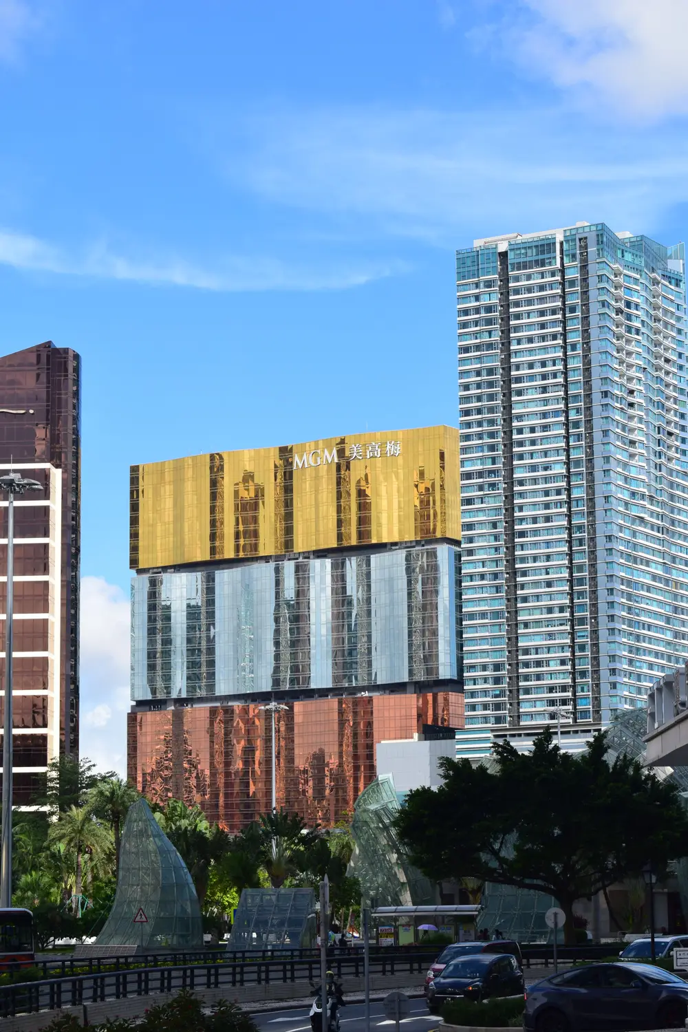 Modern glass skyscrapers with gold abstract art installation and palm trees, Macau