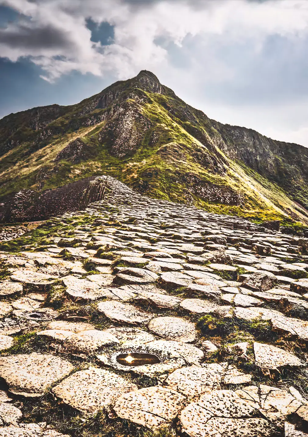 Hexagonal basalt rock columns forming a rugged coastal landscape leading up a hillside, Giant's Causeway, Ireland.