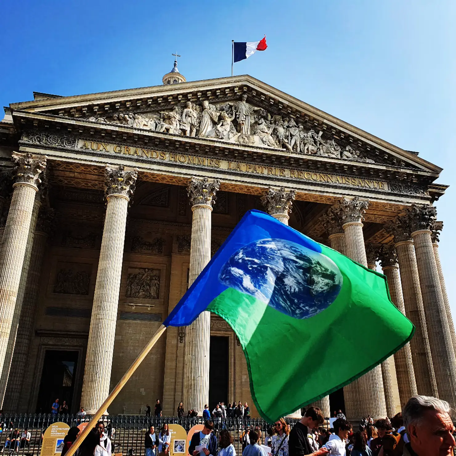 Crowd holding a green Earth flag in front of the Panthéon's columned facade in Paris