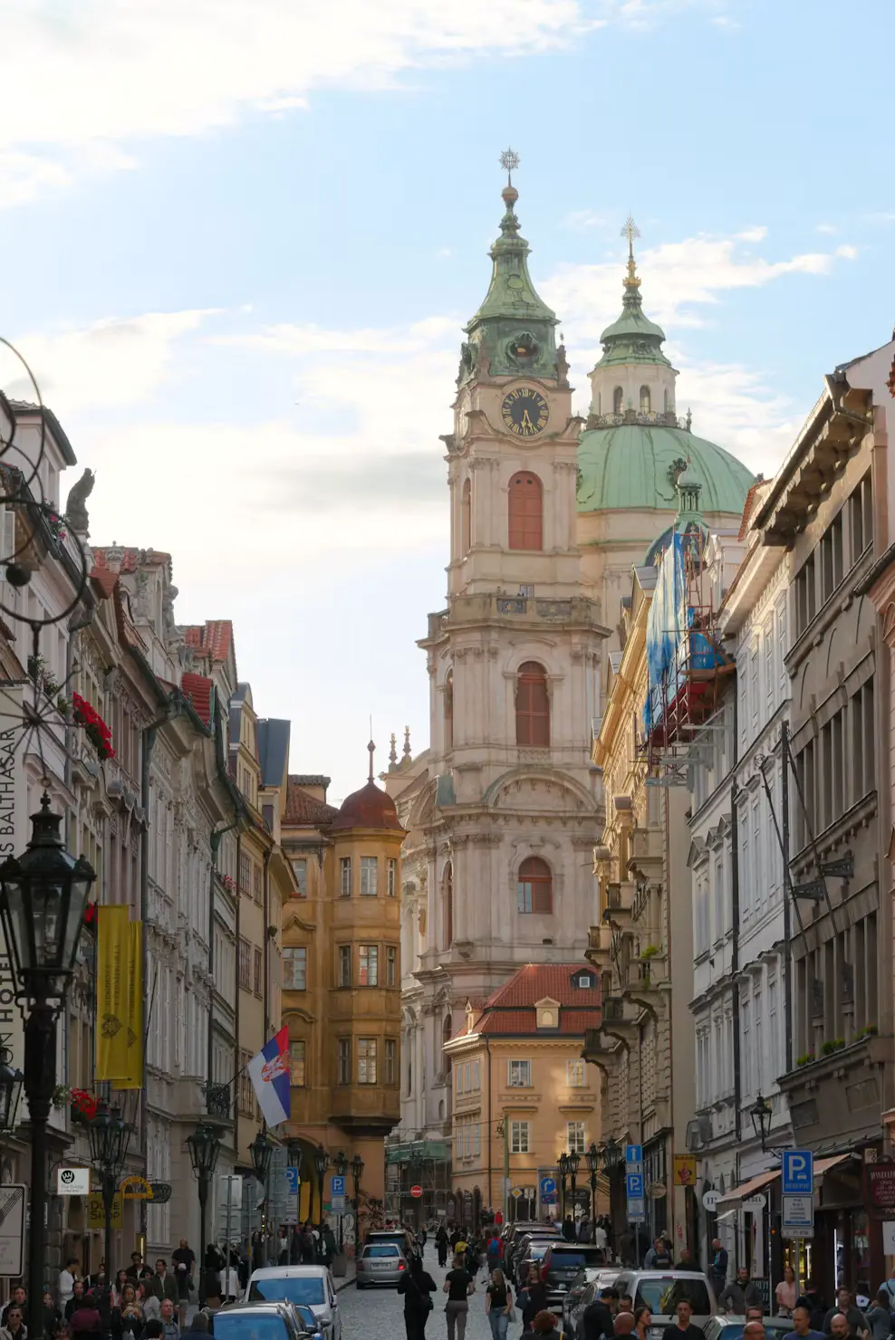 St. Nicholas Church spires rising above a busy Prague street lined with shops.