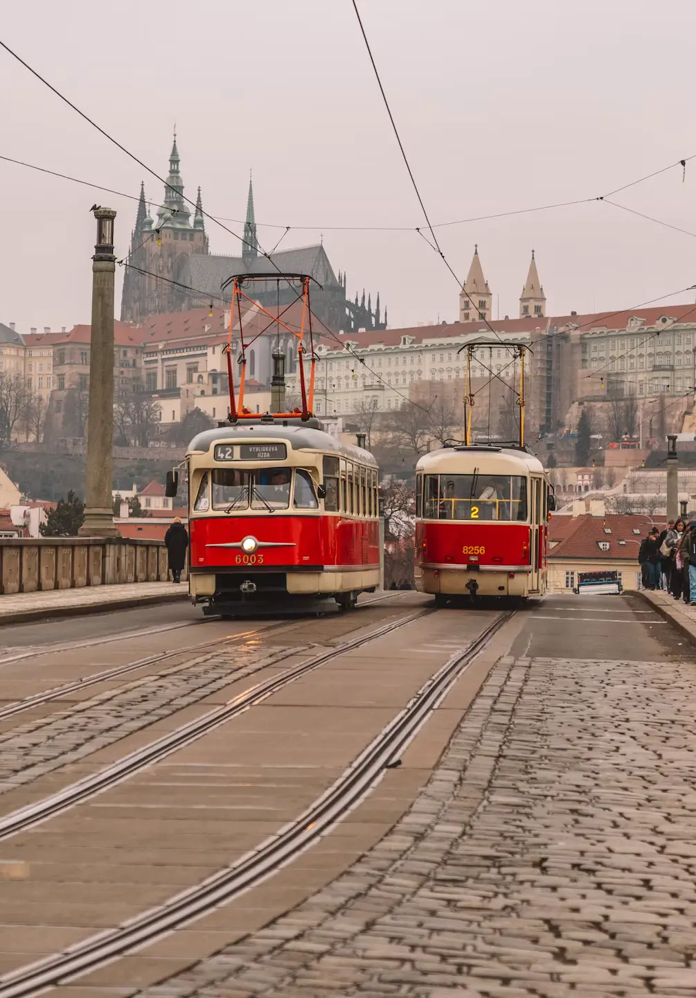 Vintage red trams on cobblestone tracks with Prague Castle visible in the distance