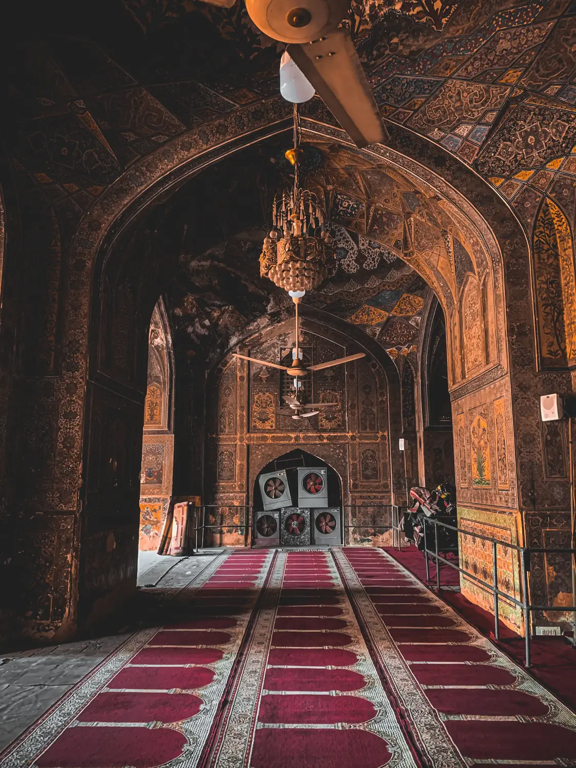 Ornate Mughal mosque interior with red carpet arched corridor and hanging lanterns Pakistan