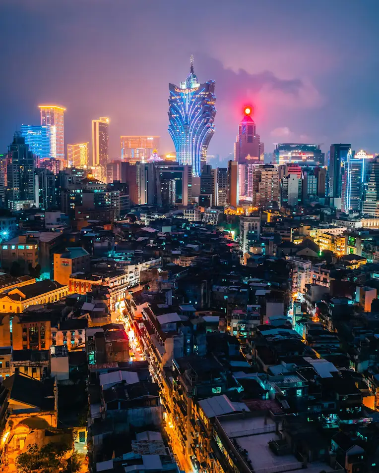 Aerial night view of Macau skyline with illuminated Grand Lisboa tower above old town rooftops