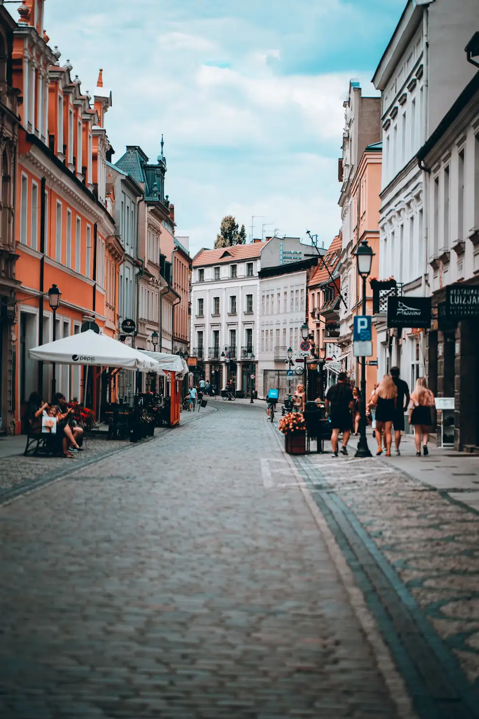 Cobblestone street lined with colorful buildings and outdoor cafés, pedestrians walking through, Poland.