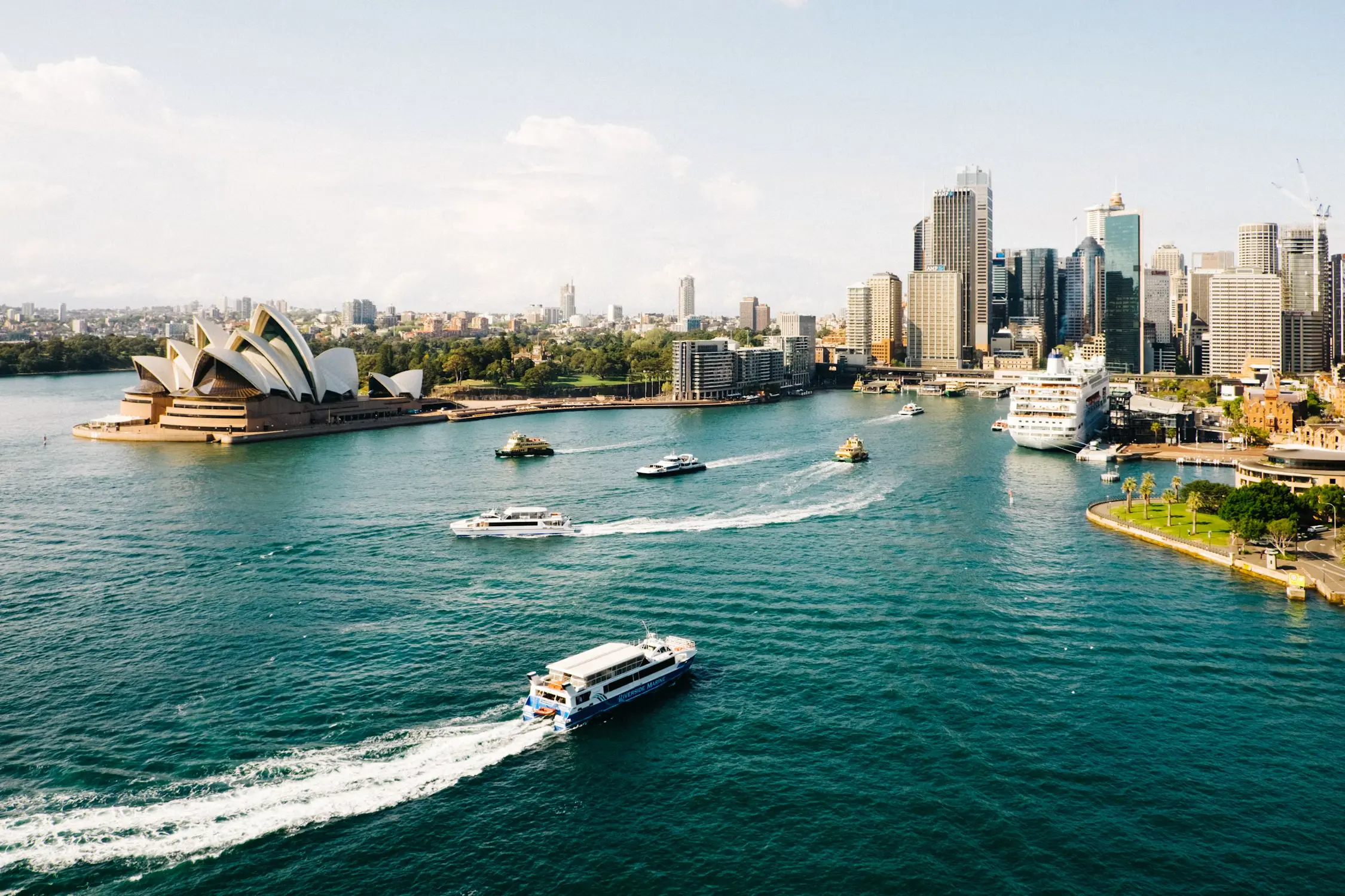 Aerial view of Sydney Harbour showing the Opera House, ferries, and city skyline on a sunny day