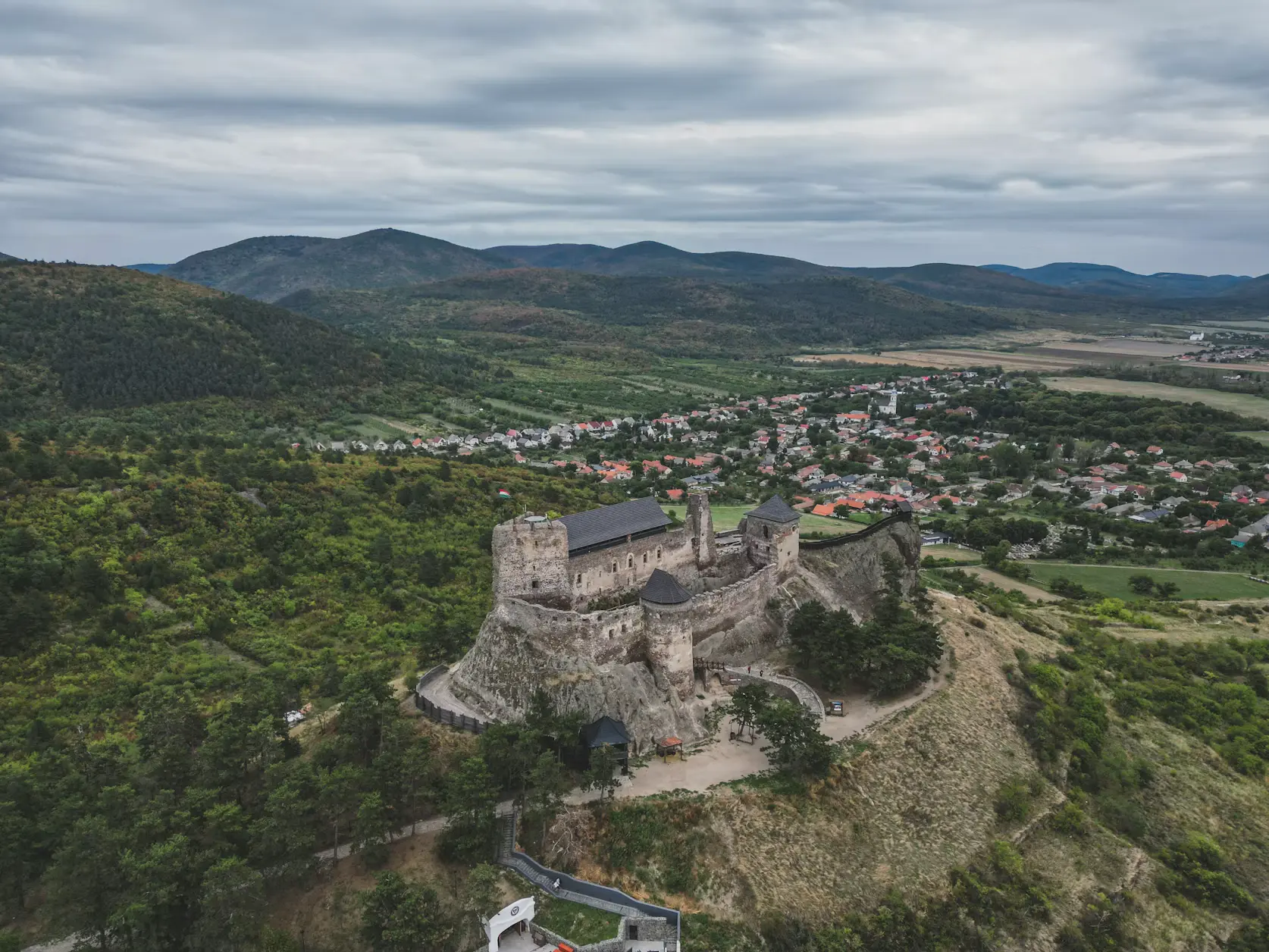 Hilltop castle ruins overlooking a village and rolling green hills.