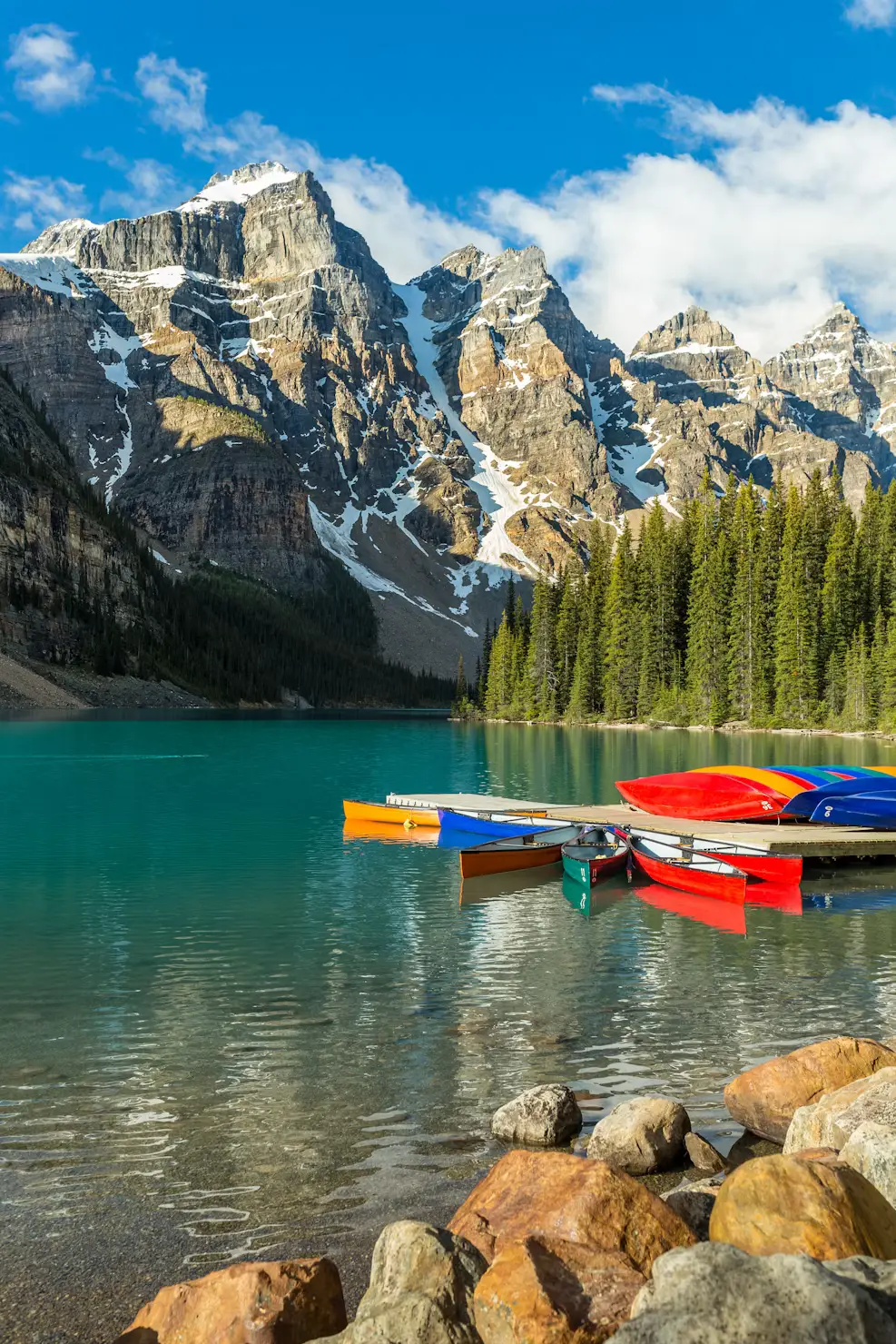 Turquoise Moraine Lake in Banff National Park with kayaks docked along the shore, framed by snow-capped mountains and forest.