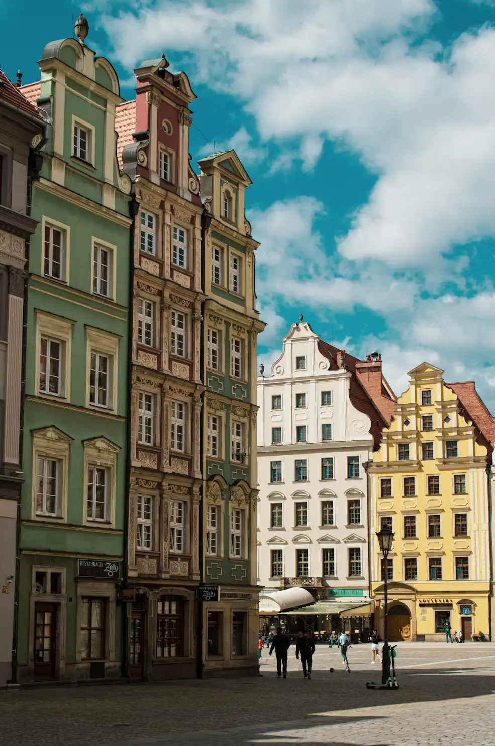 Colorful historic European buildings lining a sunny city street beneath a partly cloudy sky.
