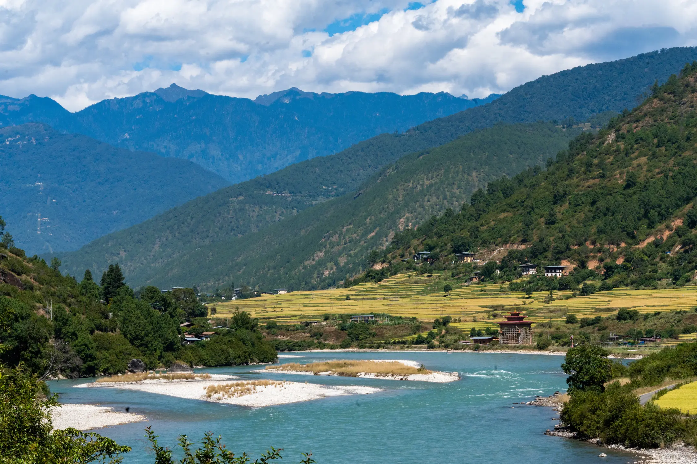 Turquoise river winding through a green Himalayan valley with terraced fields and forested mountains in Bhutan.