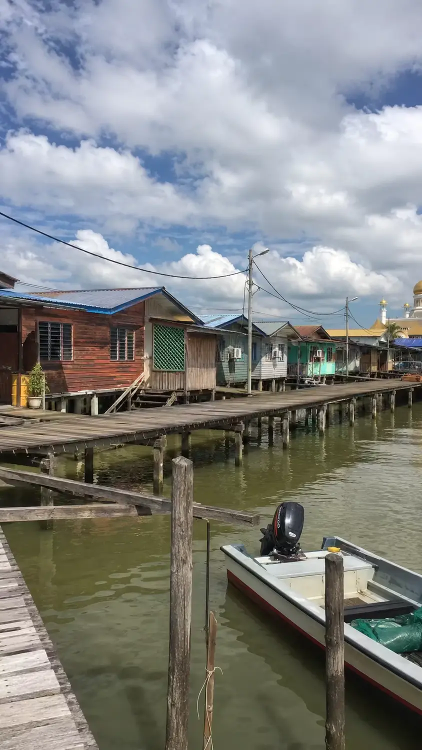 Kampong Ayer water village elevated wooden walkway and stilt houses along Brunei River with mosque in background