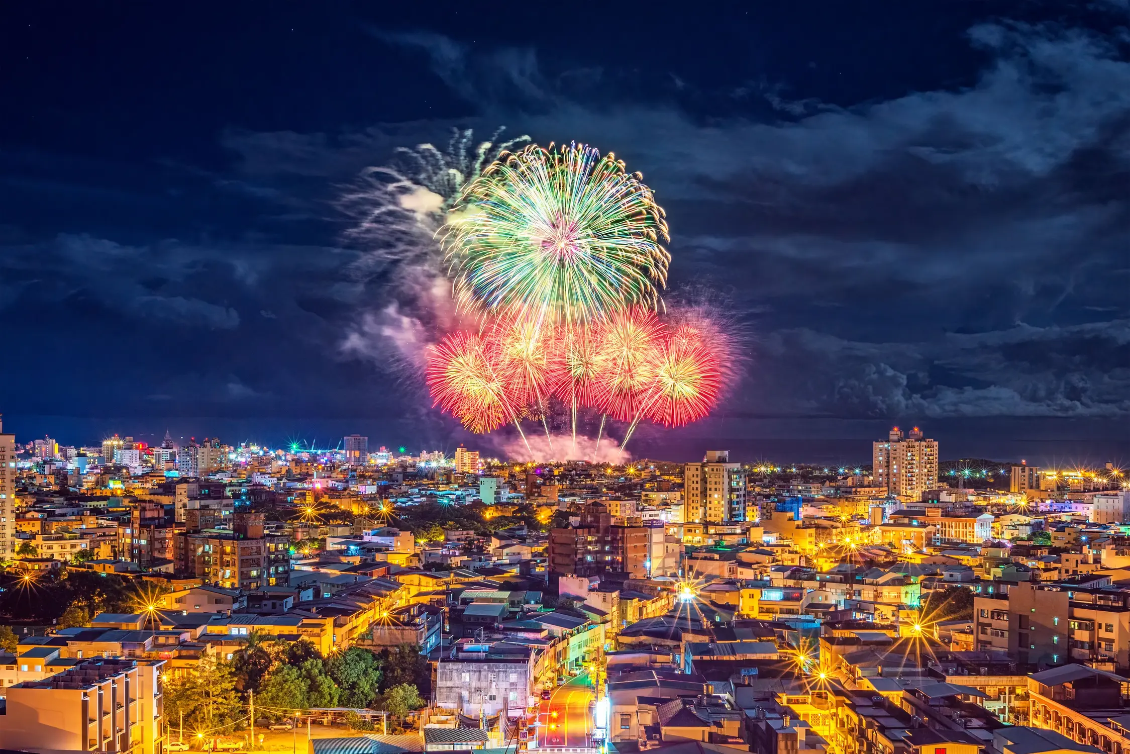 Colorful fireworks bursting in green, gold, and red over a illuminated Taiwan city skyline at night