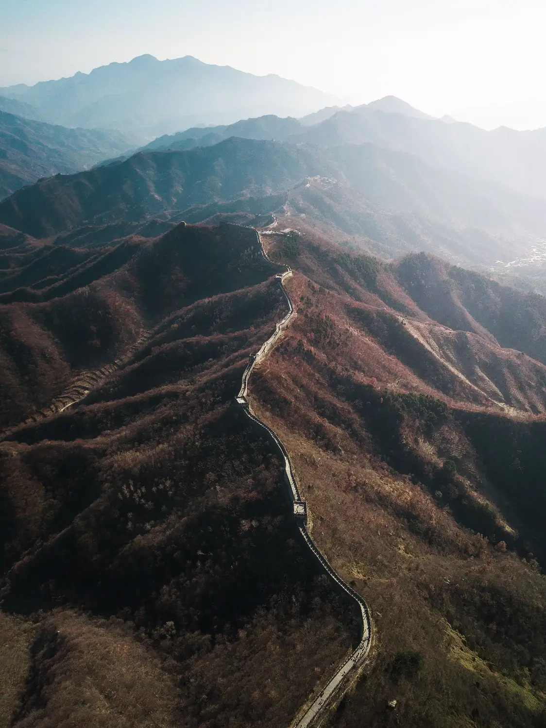 Aerial drone view of Great Wall of China winding across autumn mountain ridges in misty landscape