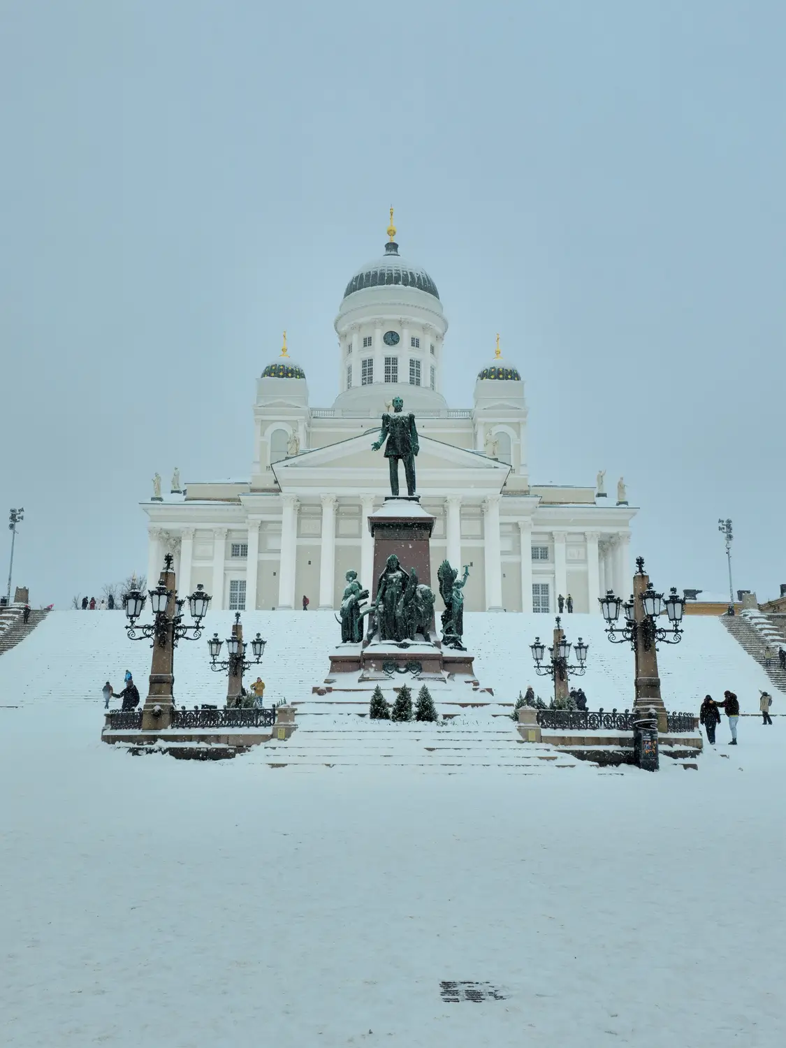 Snow-covered cathedral with a central statue and grand steps during a winter snowfall.