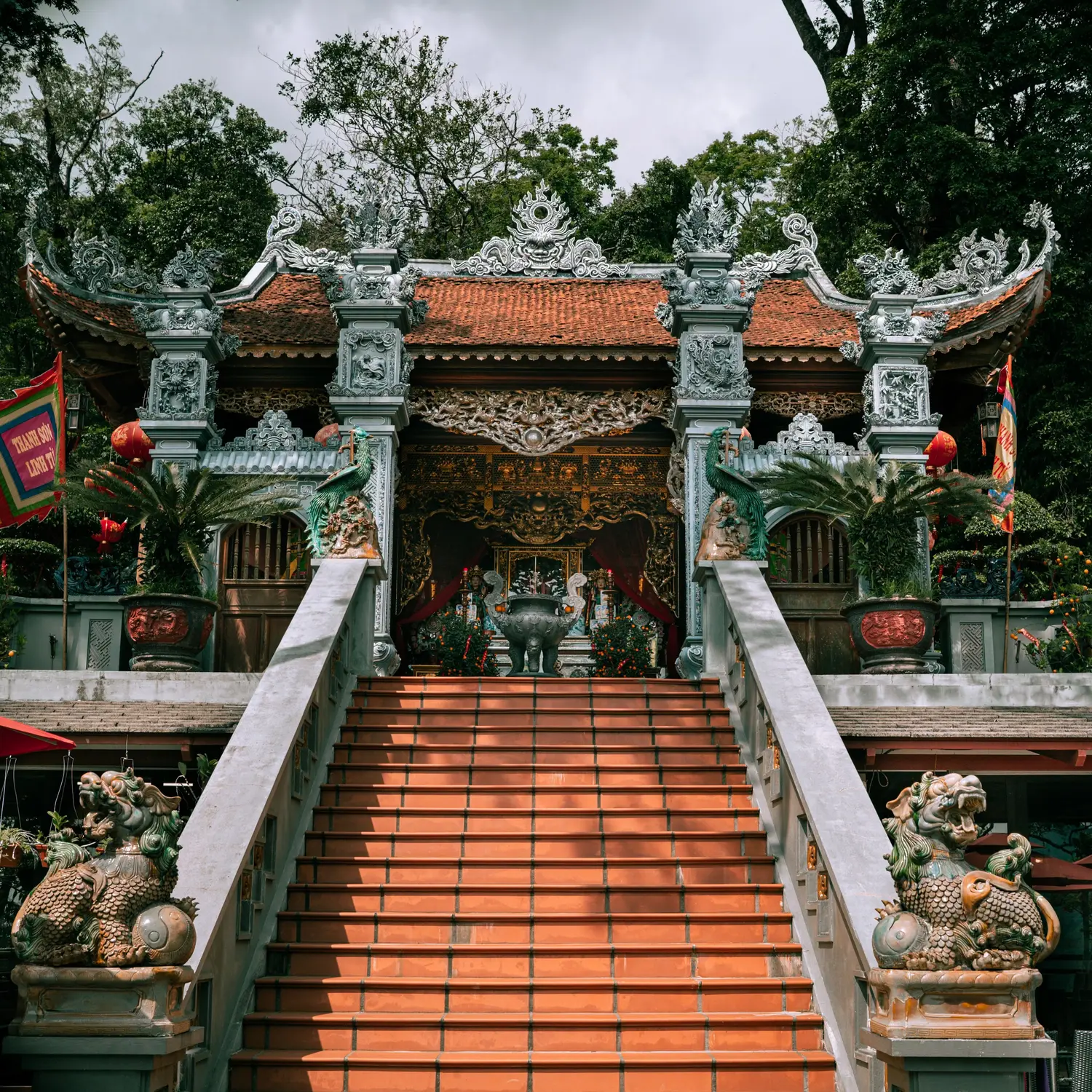 Ornately carved Vietnamese temple (Thanh Sơn Linh Từ) with a tiled roof, phoenix and dragon statues, and ceramic guardian lions flanking a wide orange-tiled staircase.