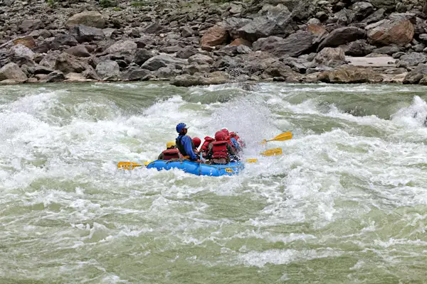 Rafters paddling through rocky whitewater rapids on a mountain river, Nepal