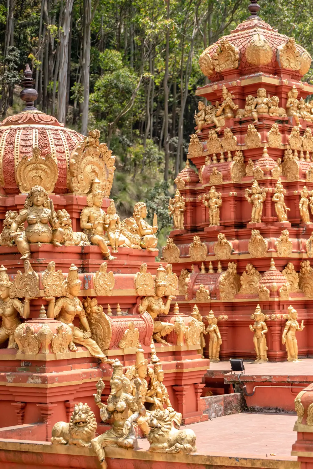 Ornate red and gold Hindu temple tower covered in intricate deity sculptures in Sri Lanka.