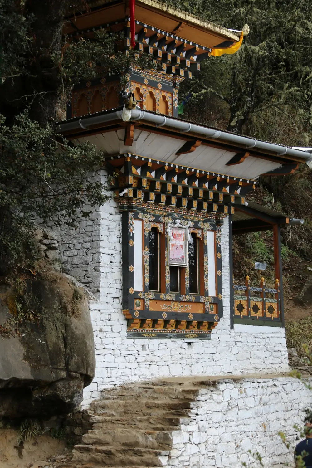 Traditional white Bhutanese chorten with ornate painted woodwork built into a rocky hillside with stone steps in Bhutan.
