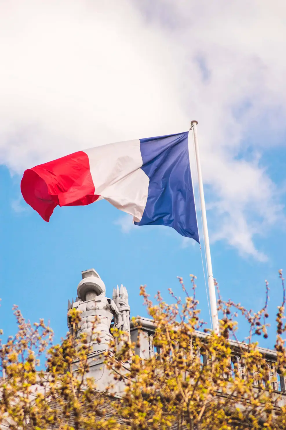 French tricolor flag waving against a blue sky above rooftops in Paris