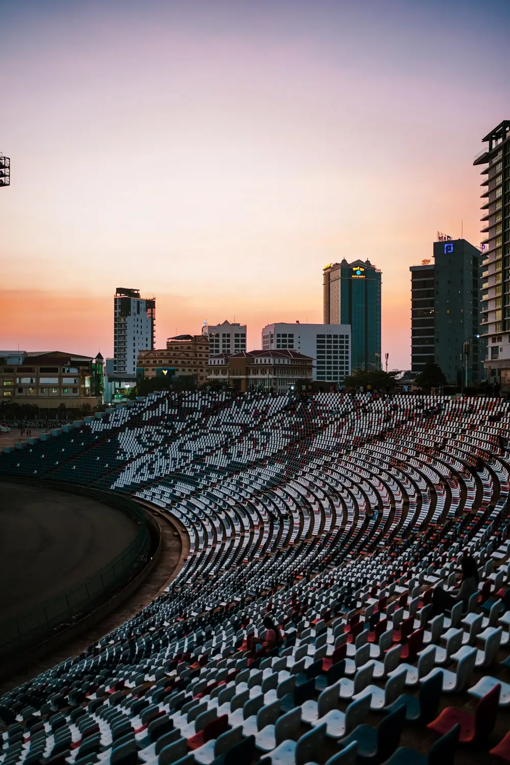 Empty stadium seats at sunset with Phnom Penh city skyline and modern high-rise buildings in background, Cambodia