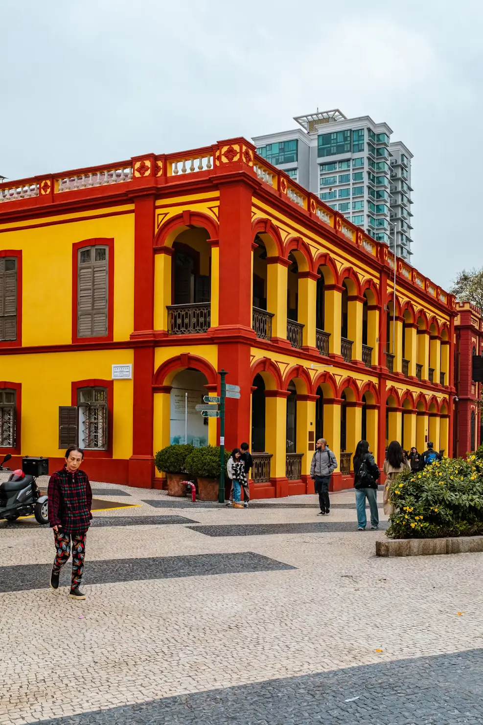 Yellow and red colonial building facade with pedestrians on cobblestone plaza, Macau