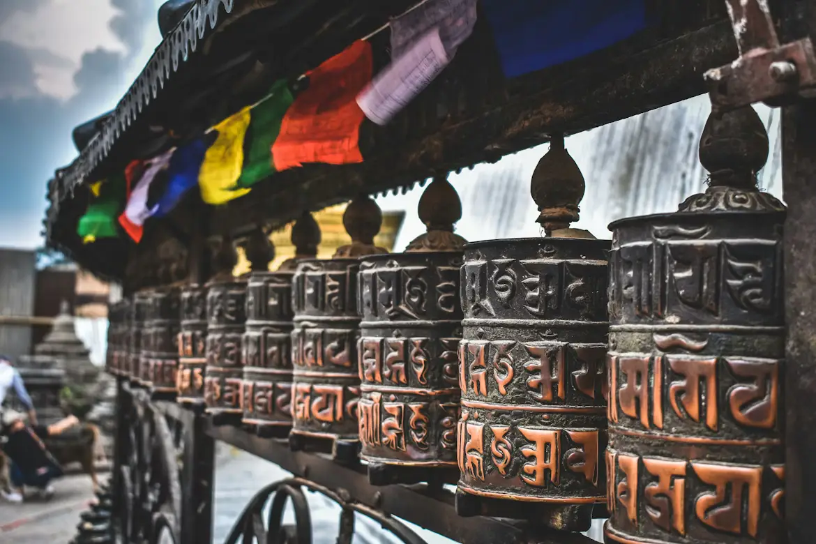 Row of golden Buddhist prayer wheels with carved inscriptions at a temple, Nepal