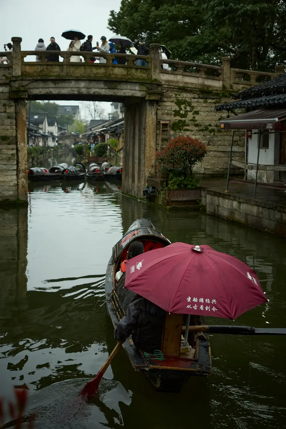 Traditional wooden rowboat with red umbrella on canal in Shaoxing water town China rainy day