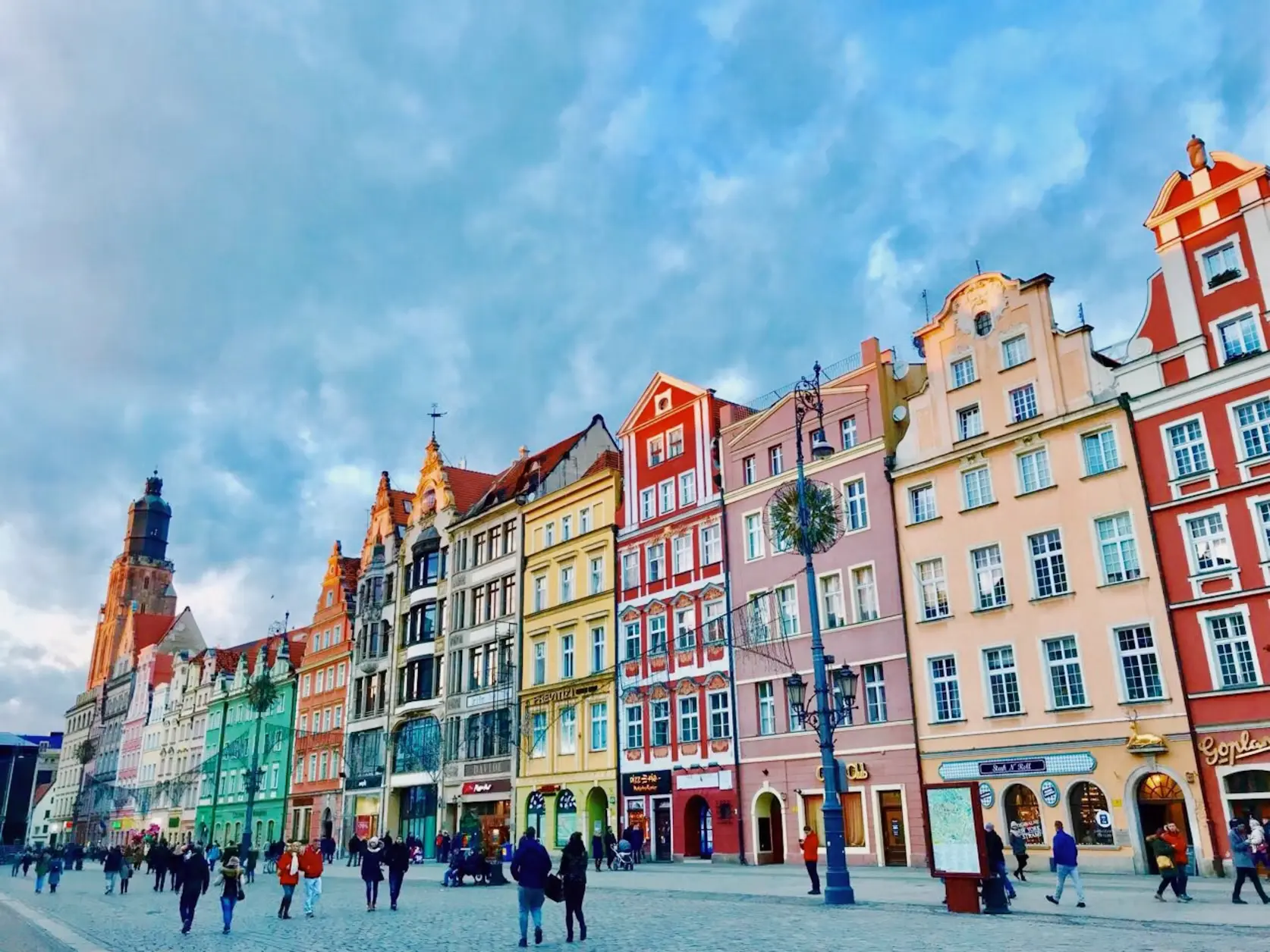 Colorful row of historic townhouses in a bustling town square filled with pedestrians, Poland.