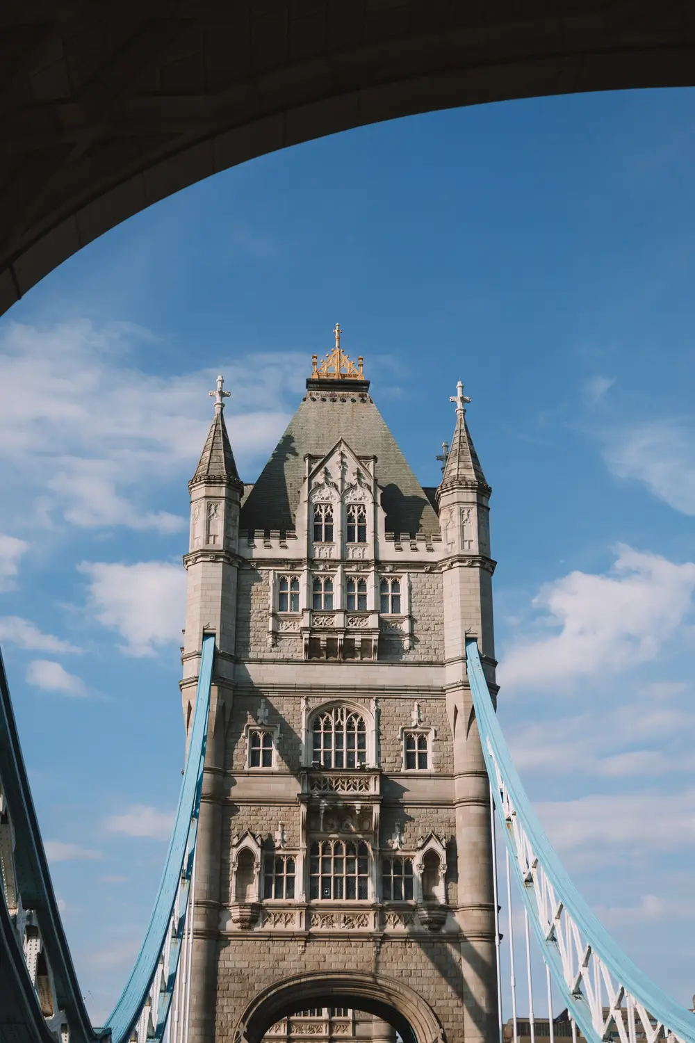 One of Tower Bridge's stone towers framed through a dark archway against a clear blue sky.