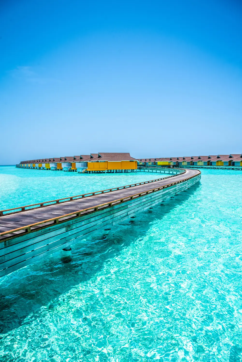View of long colorful wooden jetty extending over crystal clear turquoise shallow lagoon at Maldives resort island