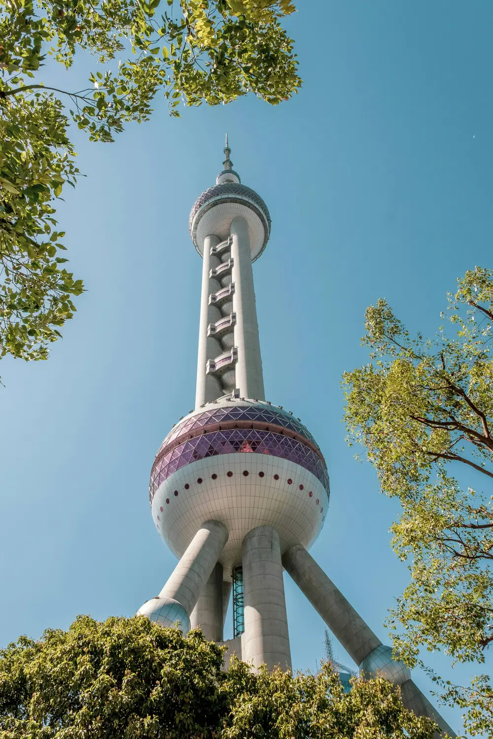 Oriental Pearl Tower Shanghai seen from below through green trees against blue sky