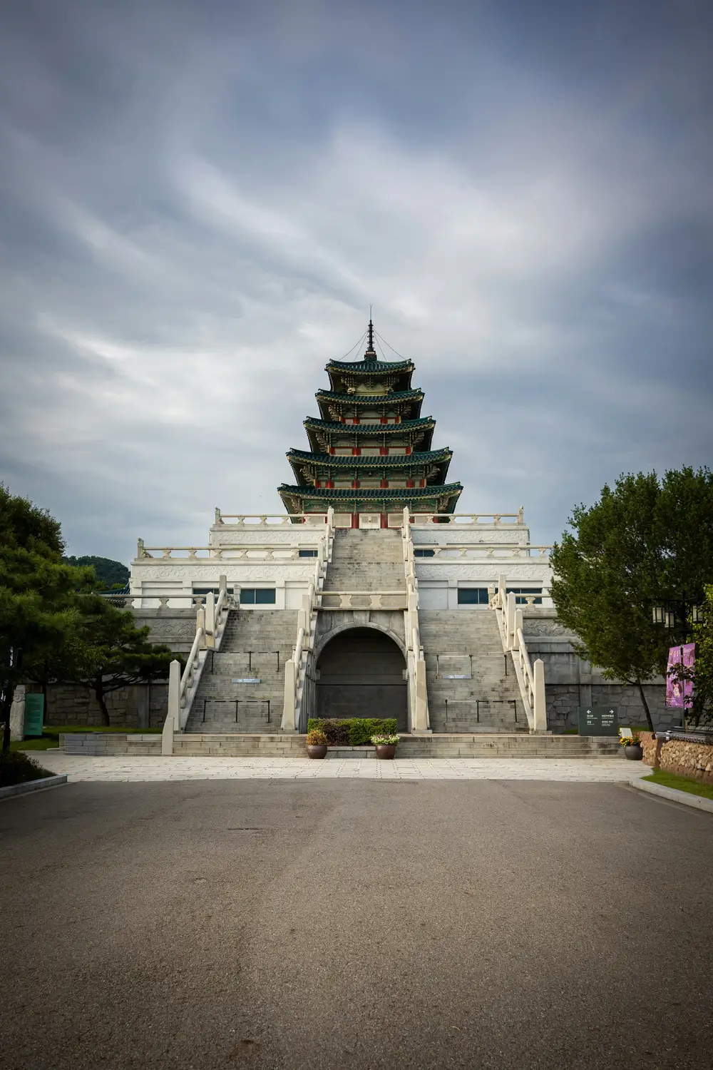 Traditional Korean palace gate with a curved tiled roof and stone bridge under a dramatic cloudy sky.