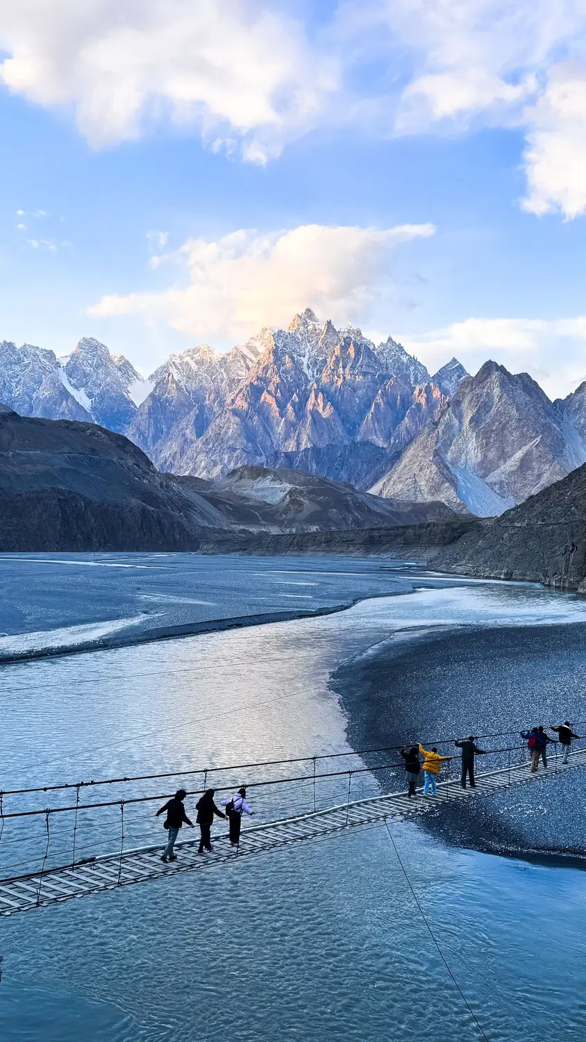 Tourists crossing Hussaini suspension bridge over Hunza River with Passu Cones peaks Pakistan