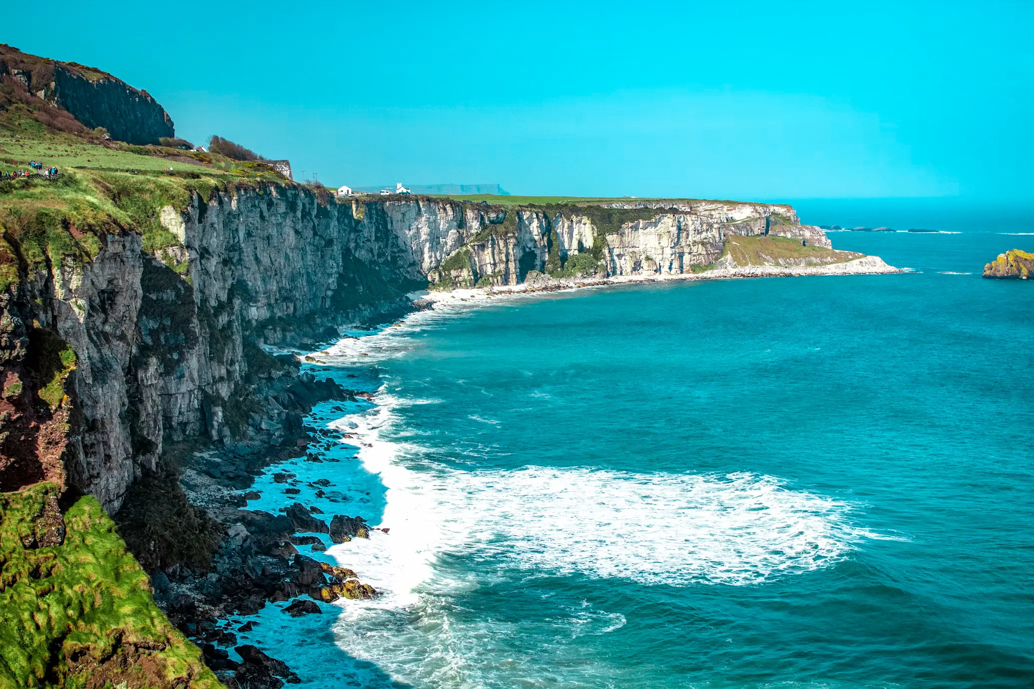 White limestone cliffs curving along a turquoise sea with waves breaking below, Ireland.