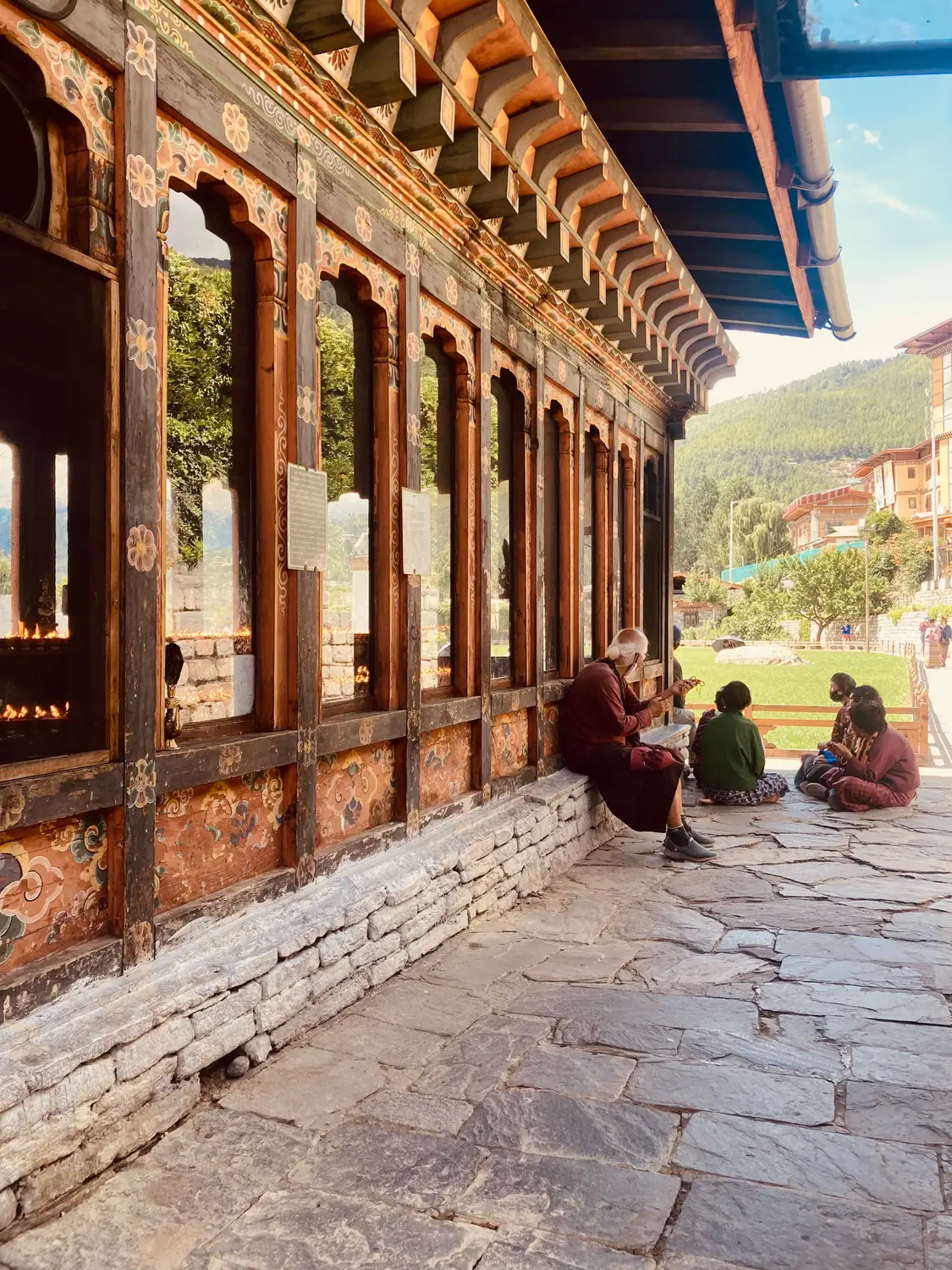 Covered walkway of a Bhutanese dzong with carved wooden columns and people resting in the shaded corridor in Bhutan.