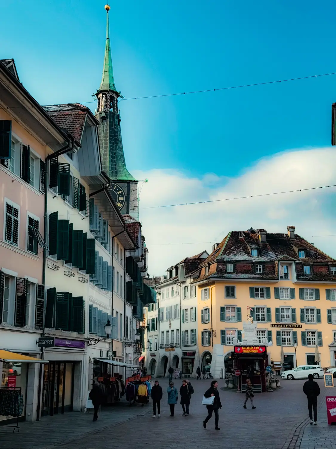 Pedestrians walking through a historic town square with a church spire, Switzerland