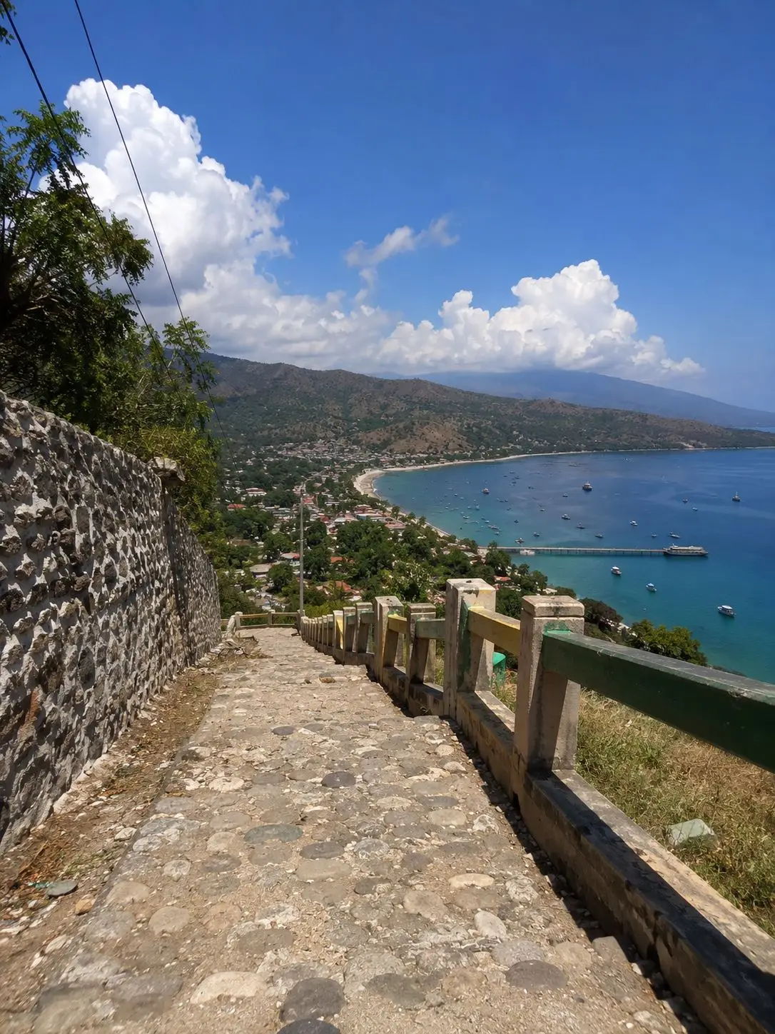 Cobblestone pathway leading down Cristo Rei hill in Dili, Timor-Leste with panoramic views of Dili Bay, turquoise Timor Sea, and the city coastline stretching along the hillside