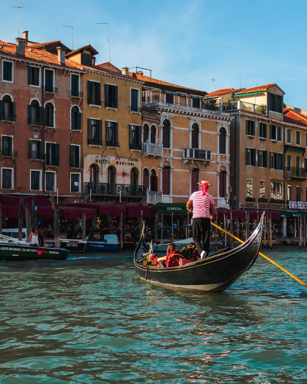 Gondolier navigating a narrow canal between colorful buildings in Venice