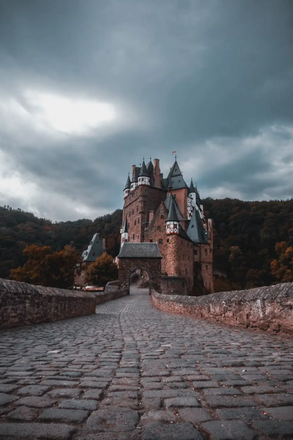 Cobblestone bridge leading to Eltz Castle under a moody, overcast sky