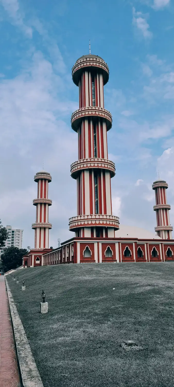 Distinctive red and white striped minarets of Baitul Mukarram National Mosque with arched facade against blue sky, Dhaka, Bangladesh
