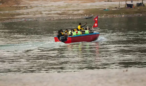 Red raft carrying people down a wide river with the Nepali flag, Nepal