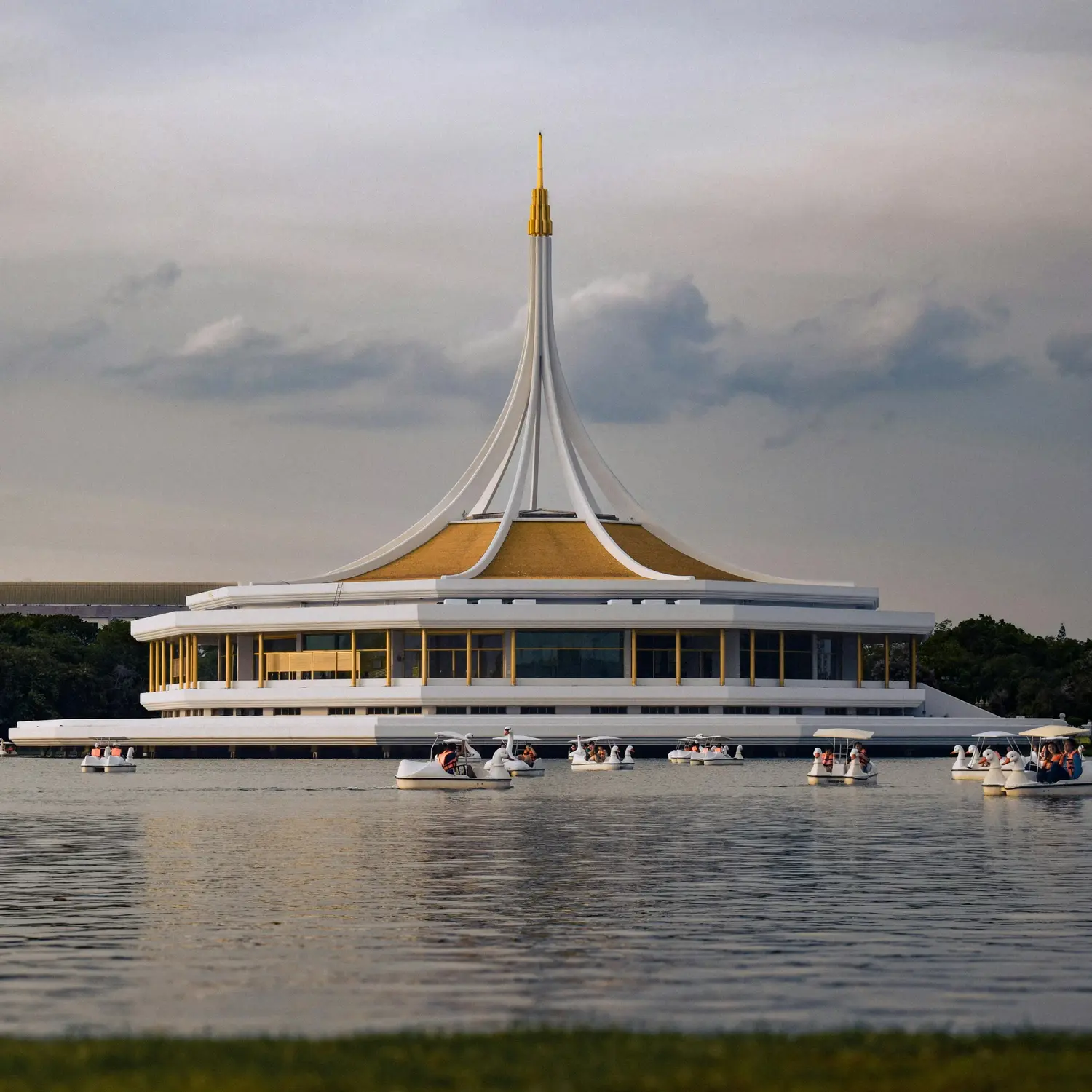 Ratchamangkhala Pavilion with its spire-topped roof at Suan Luang Rama IX Park, Bangkok, with swan paddle boats on the lake at dusk