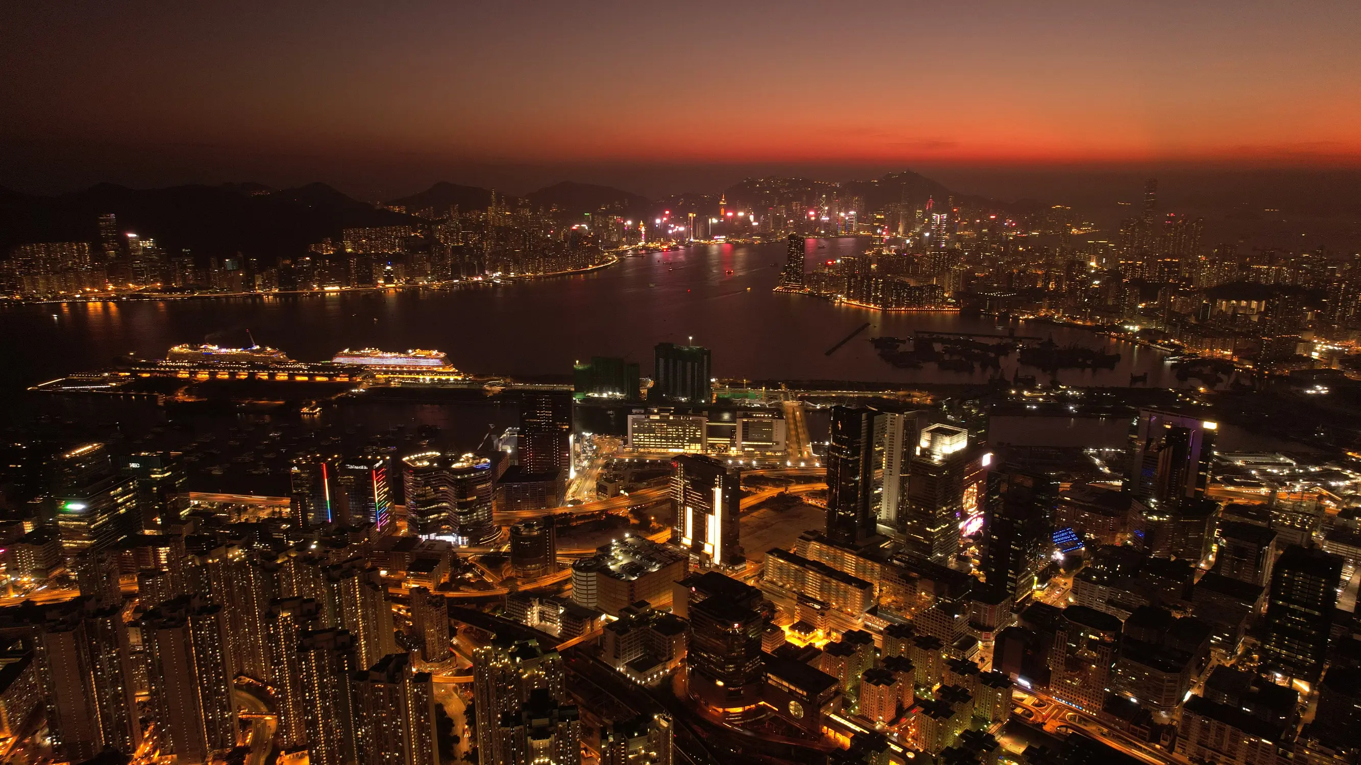 Aerial panorama of Hong Kong's illuminated skyline and harbour at sunset with glowing city lights in Hong Kong.