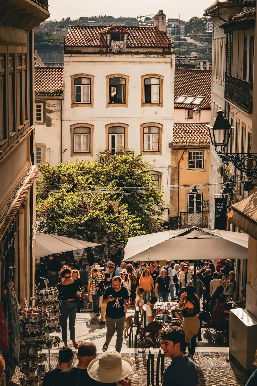 Crowded pedestrian street lined with historic buildings, outdoor café seating, and market stalls beneath terracotta rooftops.